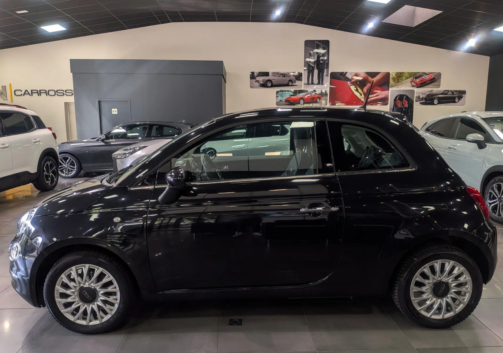 Profil côté gauche d'une FIAT 500 1.2 69 CH LOUNGE noire Crossover Black dans un showroom lumineux.