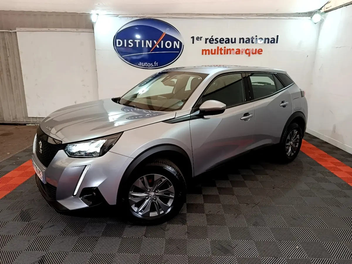 Peugeot 2008 gris clair vue 3/4 avant droit dans un showroom avec éclairage et logo Distinxion en arrière-plan