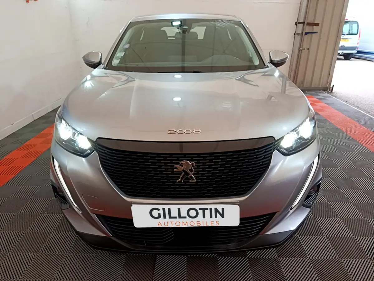 Vue de face d'une Peugeot 2008 gris clair avec phares LED allumés dans un garage fermé.