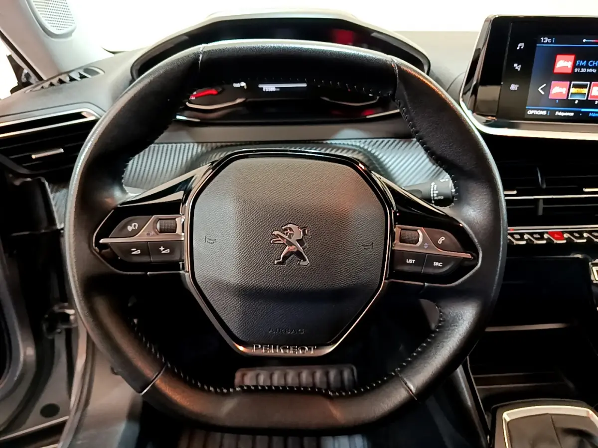 Volant cuir noir Peugeot 2008 2020 vu de face avec commandes intégrées et tableau de bord numérique en arrière-plan.