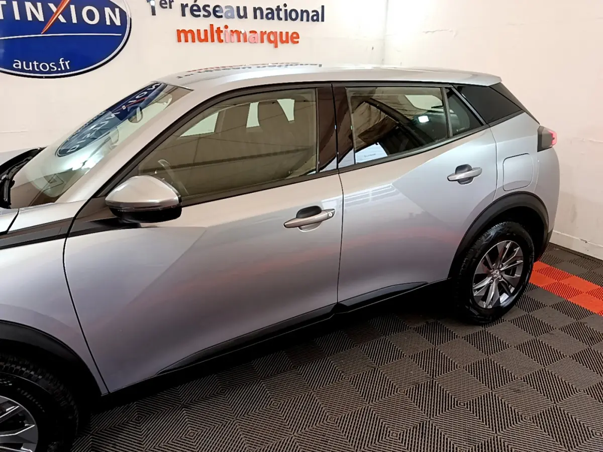 Profil côté gauche d'un Peugeot 2008 gris clair 2020 avec jantes alliage et rétroviseurs noirs dans un showroom.