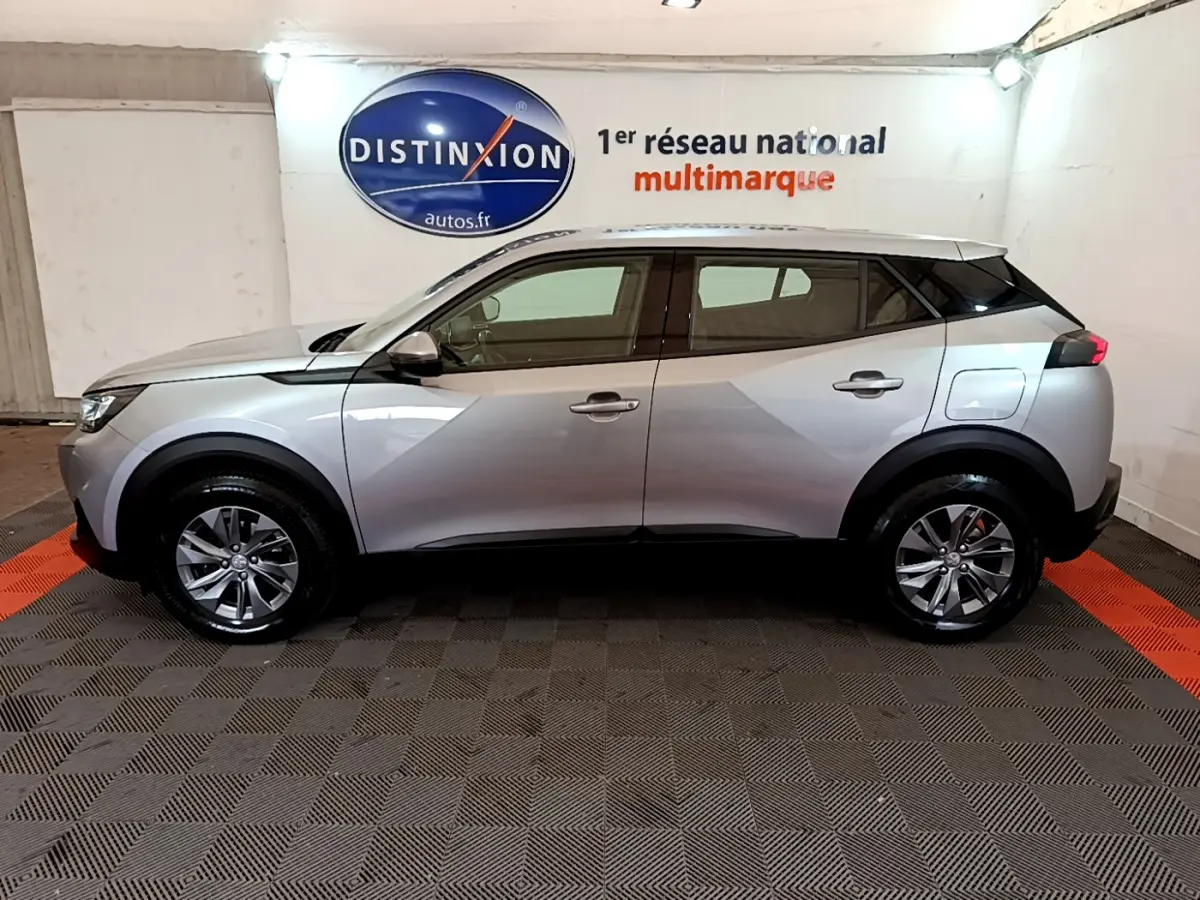 Profil côté gauche d'un Peugeot 2008 gris clair 2020 en showroom avec jantes alliage et toit noir contrasté.