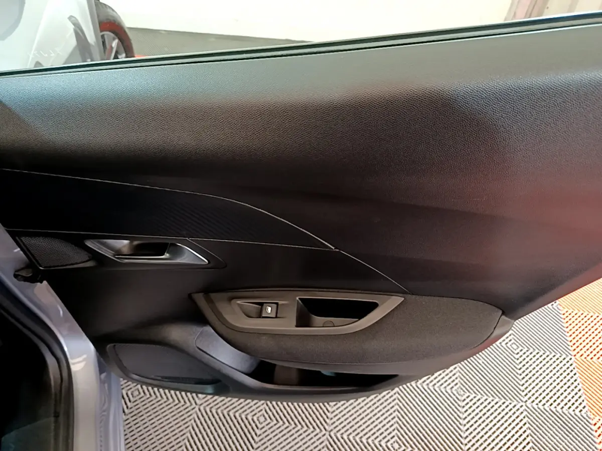 Intérieur de la porte côté gauche d'une Peugeot 2008 gris clair, avec commande de vitre et poignée intégrée.