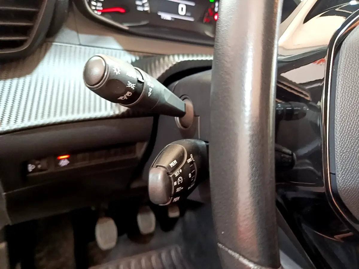 Gros plan sur les commandes derrière le volant cuir noir du Peugeot 2008 gris clair, tableau de bord texturé visible.