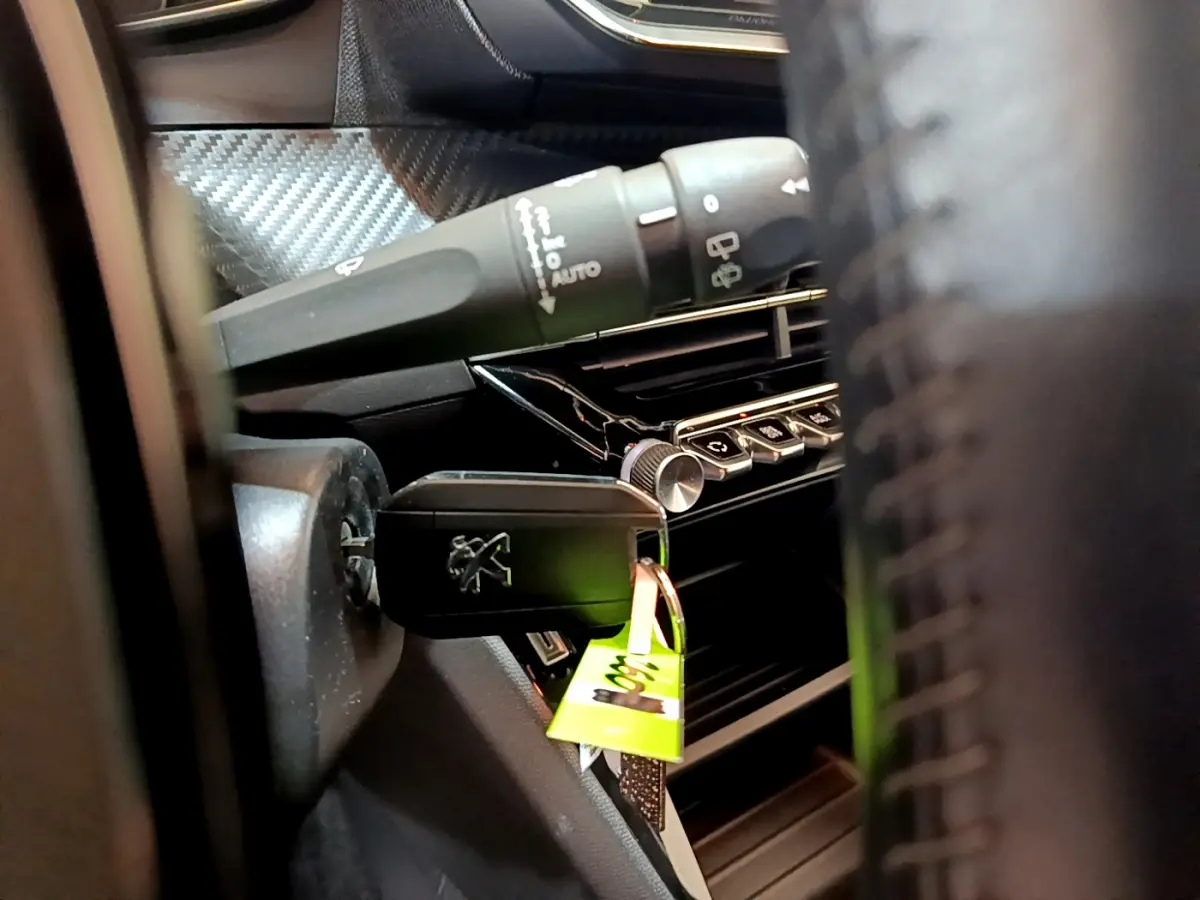 Gros plan sur la clé Peugeot insérée dans le contacteur, avec partie du tableau de bord et commandes visibles.