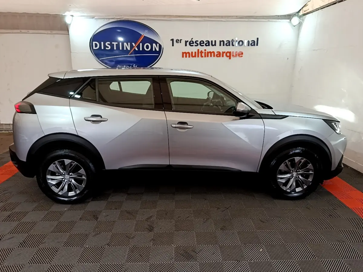 Profil côté droit d'un Peugeot 2008 gris clair 2020 dans un showroom avec logo Distinxion en arrière-plan.