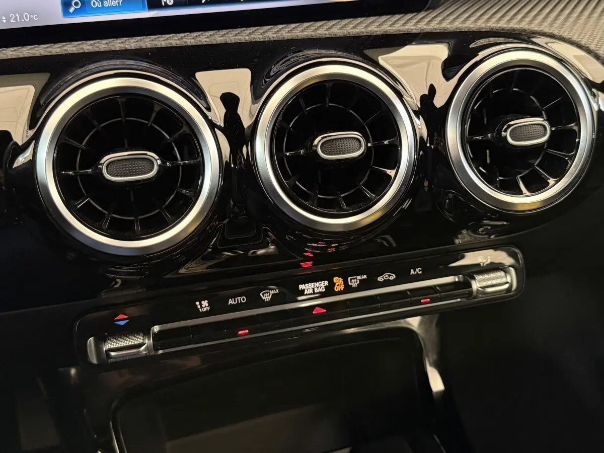 Gros plan sur la sortie d’air circulaire chromée et la commande de climatisation du tableau de bord noir brillant d’une Mercedes Classe A 180 d.