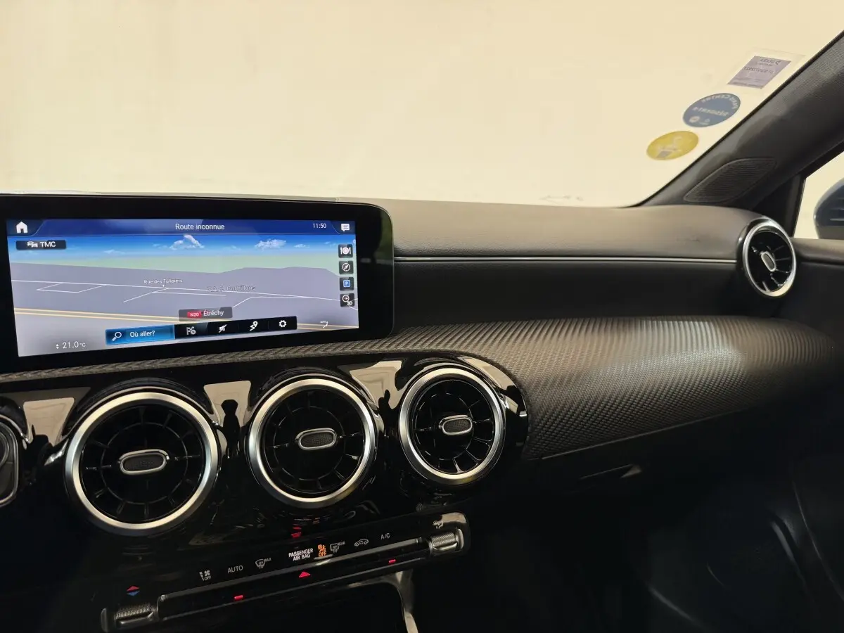 Vue intérieure côté passager du tableau de bord noir avec écran tactile large et aérateurs ronds chromés d'une Mercedes Classe A 180 d.