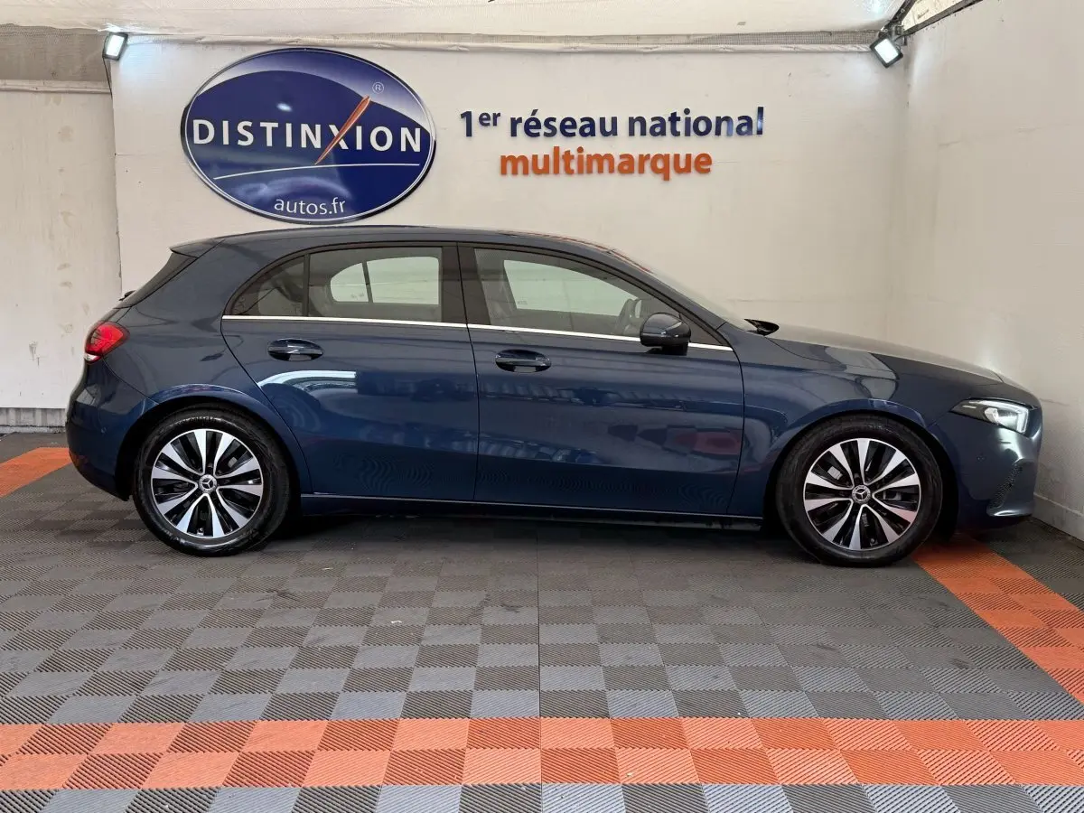 Vue de profil côté gauche d'une Mercedes Classe A 180 d Business Line bleu dans un showroom avec logo Distinxion en arrière-plan.