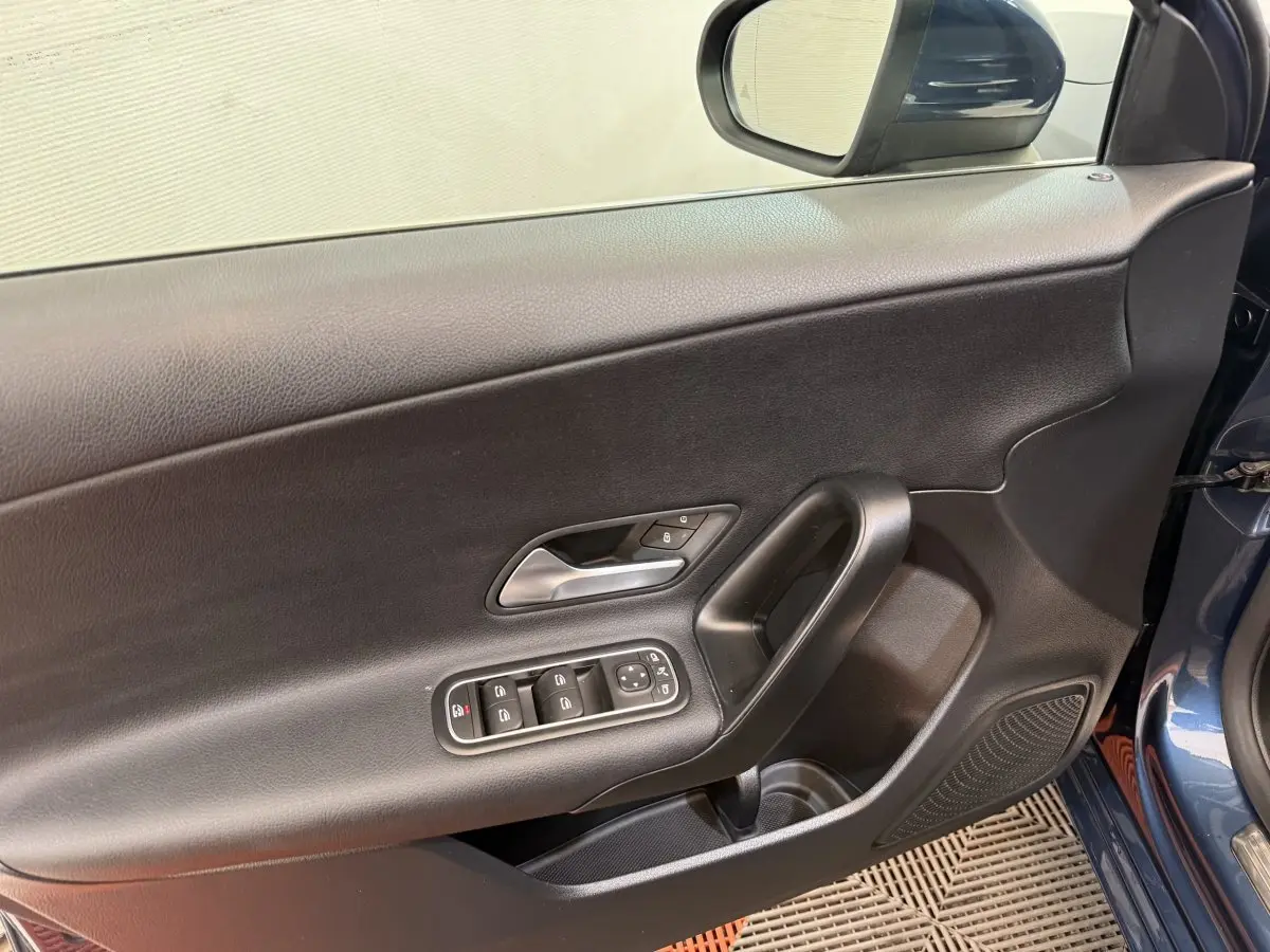 Vue intérieure côté conducteur de la porte d’une Mercedes Classe A 180 d Business Line bleu, avec commandes électriques et poignée noire.