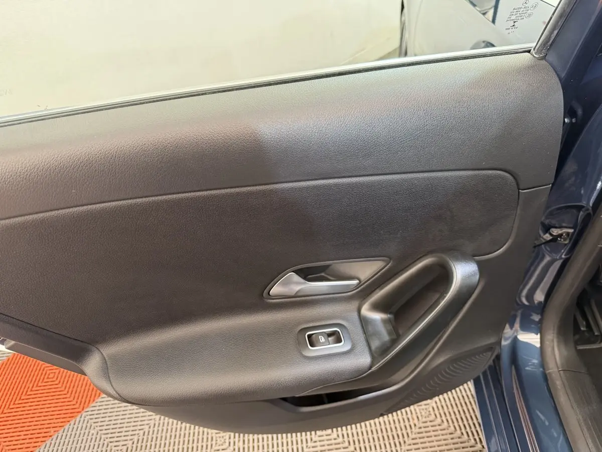 Vue rapprochée de la porte côté gauche d'une Mercedes Classe A 180 d Business Line bleu, avec poignée et bouton de vitre électrique.