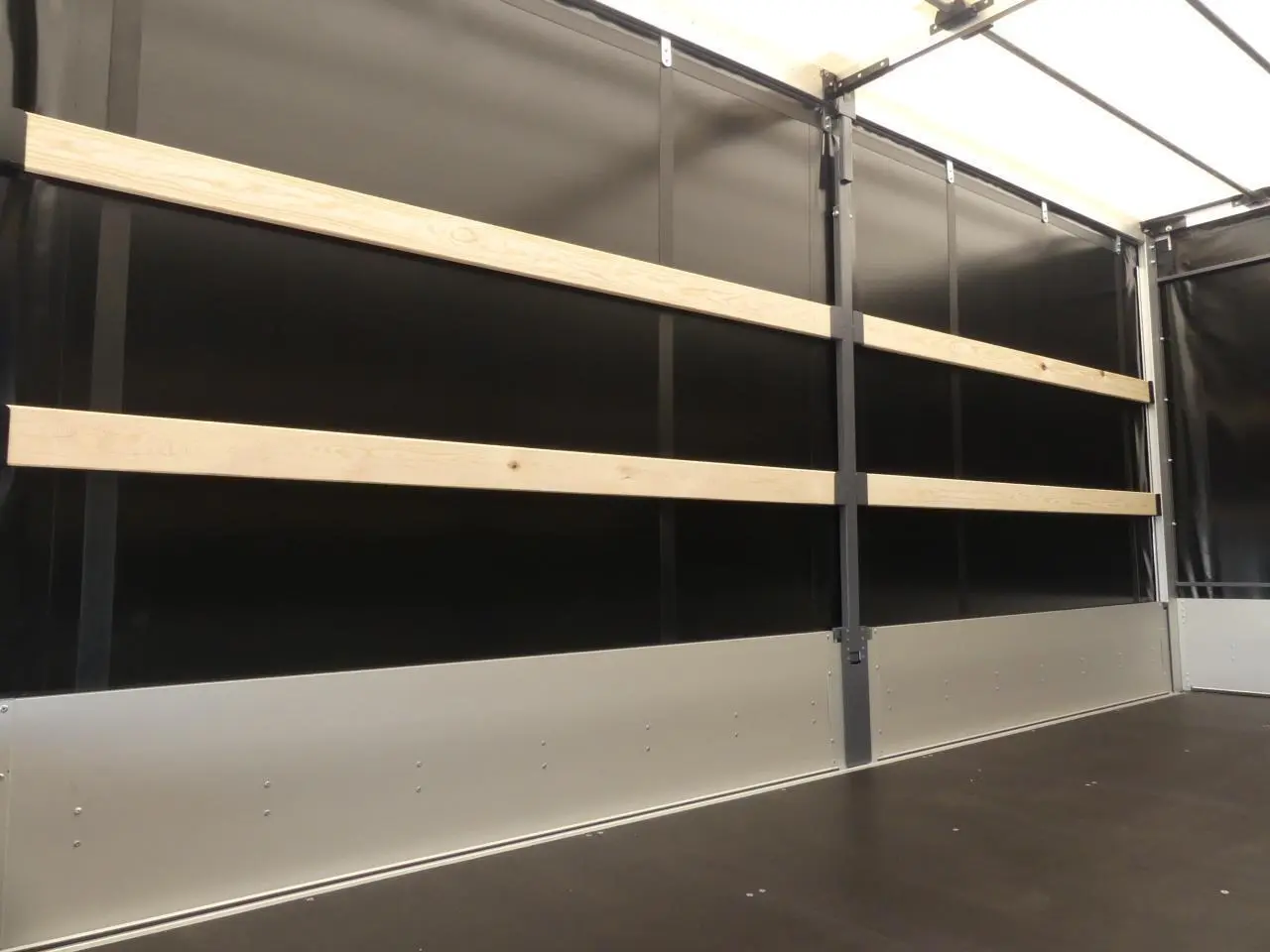 Vue intérieure du Renault Master Extra 2025 gris, montrant la bâche noire avec renforts en bois et plancher foncé.