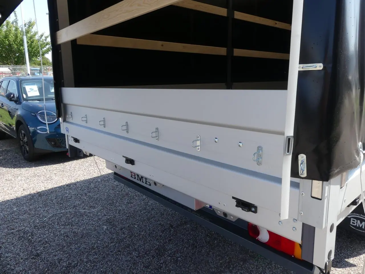 Vue arrière du Renault Master Extra gris avec bâche noire et ridelles métalliques blanches ouvertes sur un sol gravillonné.