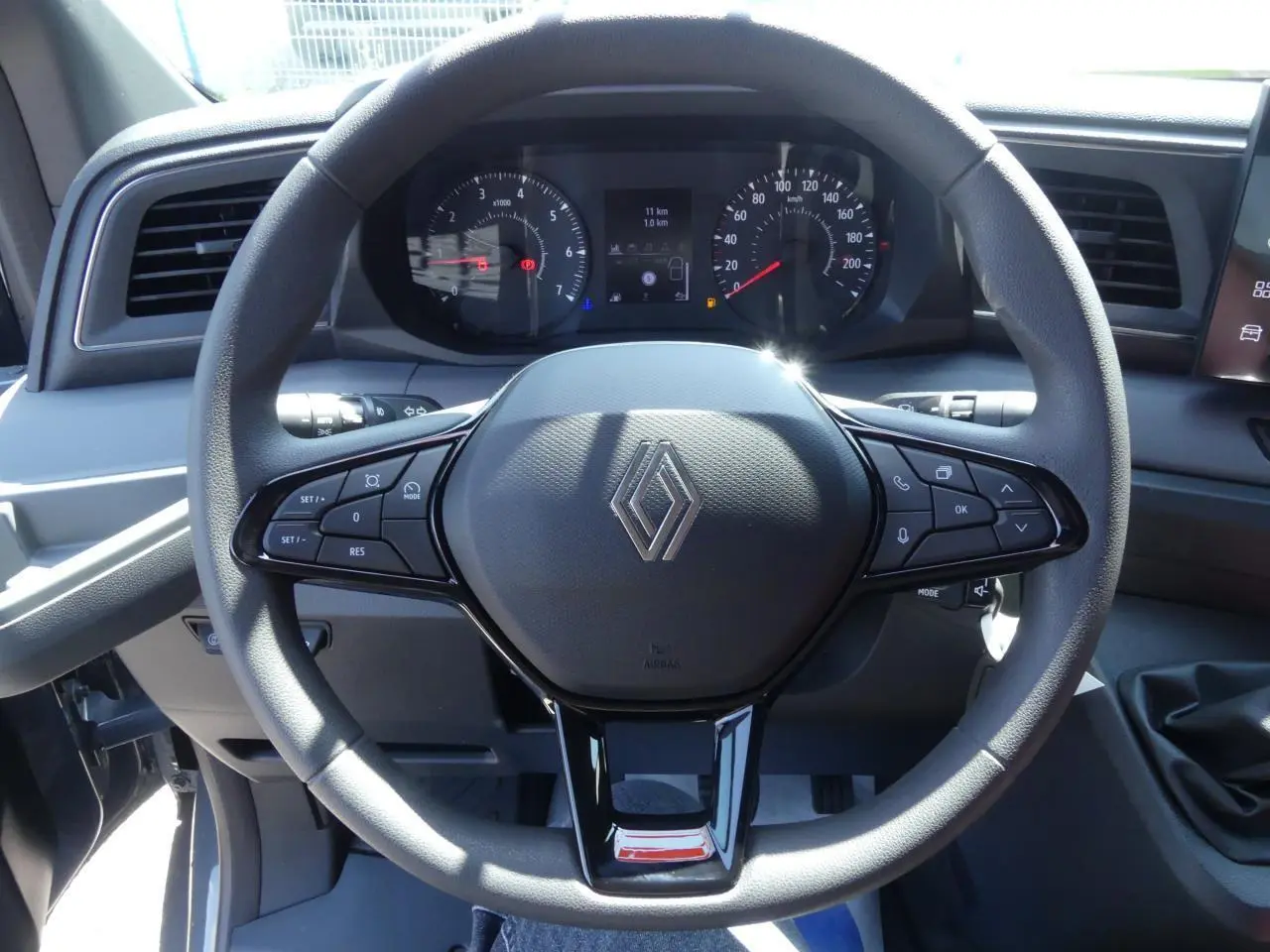 Vue rapprochée du volant noir du Renault Master 2025 avec commandes intégrées et tableau de bord digital en arrière-plan.