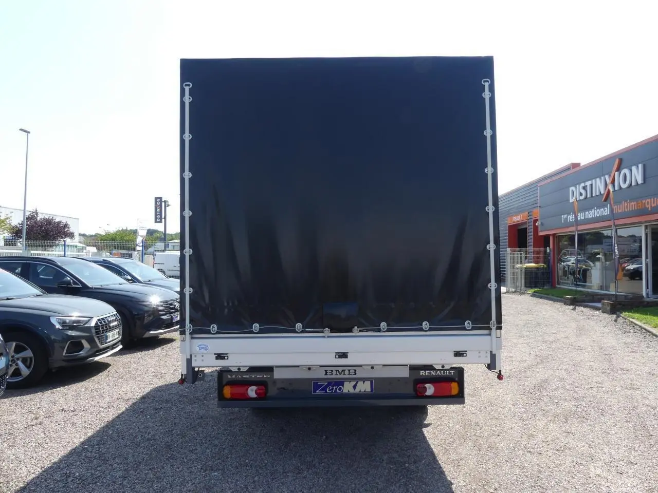 Vue arrière d'un Renault Master Extra gris avec bâche noire et feux arrière visibles sur un parking.