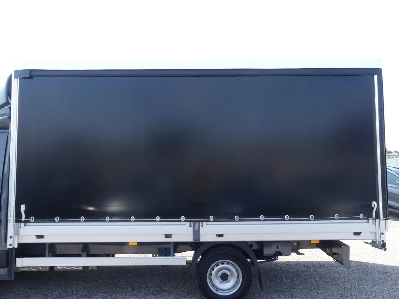 Profil latéral droit du Renault Master Extra 2025 gris avec bâche noire couvrant la zone de chargement.