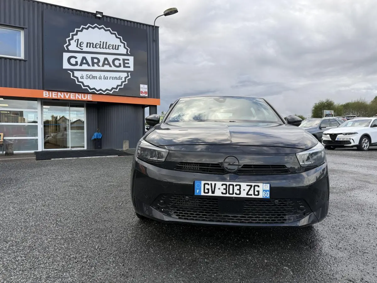 Opel Corsa noire vue de face, calandre Vizor et plaque d'immatriculation française visible devant un garage.