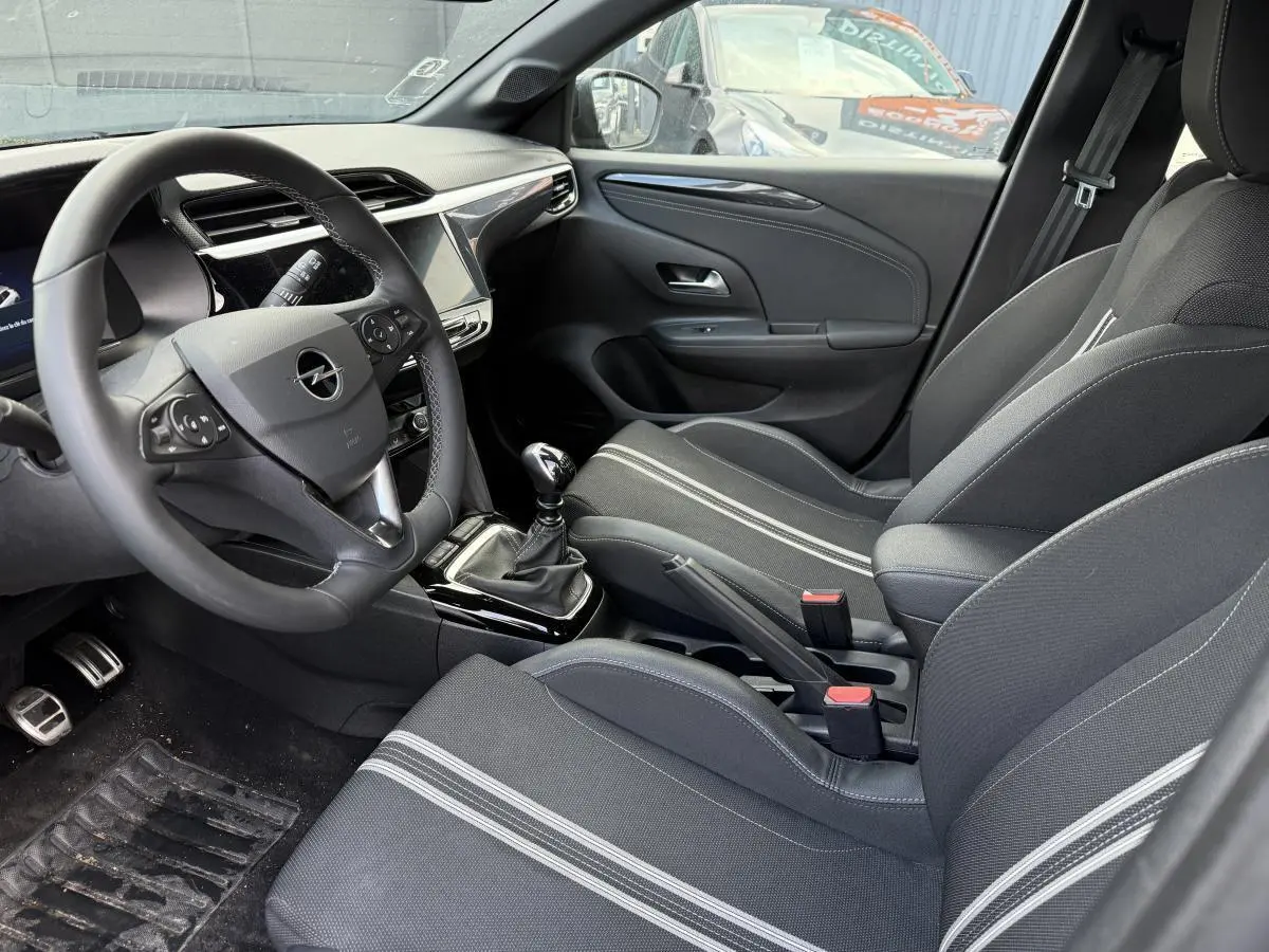Intérieur avant droit de l'Opel Corsa noir 2024 avec sièges sport tissu noir et blanc et volant multifonction.