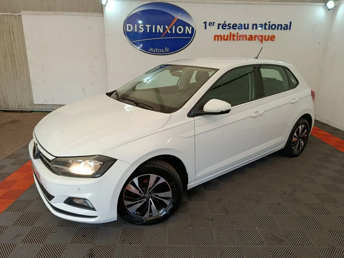 Volkswagen Polo blanche vue en 3/4 avant droit, avec phares allumés et jantes alliage distinctives.