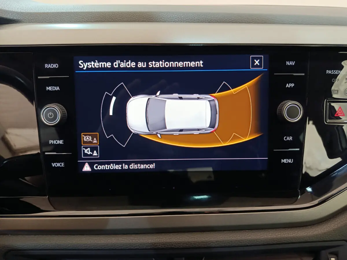 Écran tactile intérieur affichant l'aide au stationnement d'une Volkswagen Polo blanche vue de dessus.