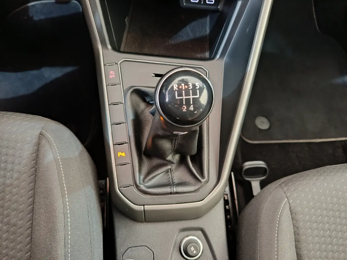 Gros plan sur le levier de vitesses manuel noir entouré des sièges avant gris du Volkswagen Polo 1.0 TSI 2020.