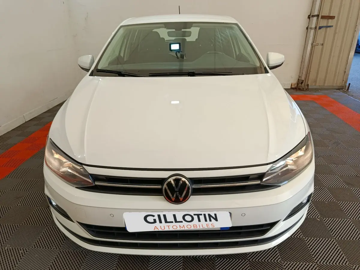 Vue avant d'une Volkswagen Polo blanche 2020 avec calandre noire et phares allumés en intérieur.
