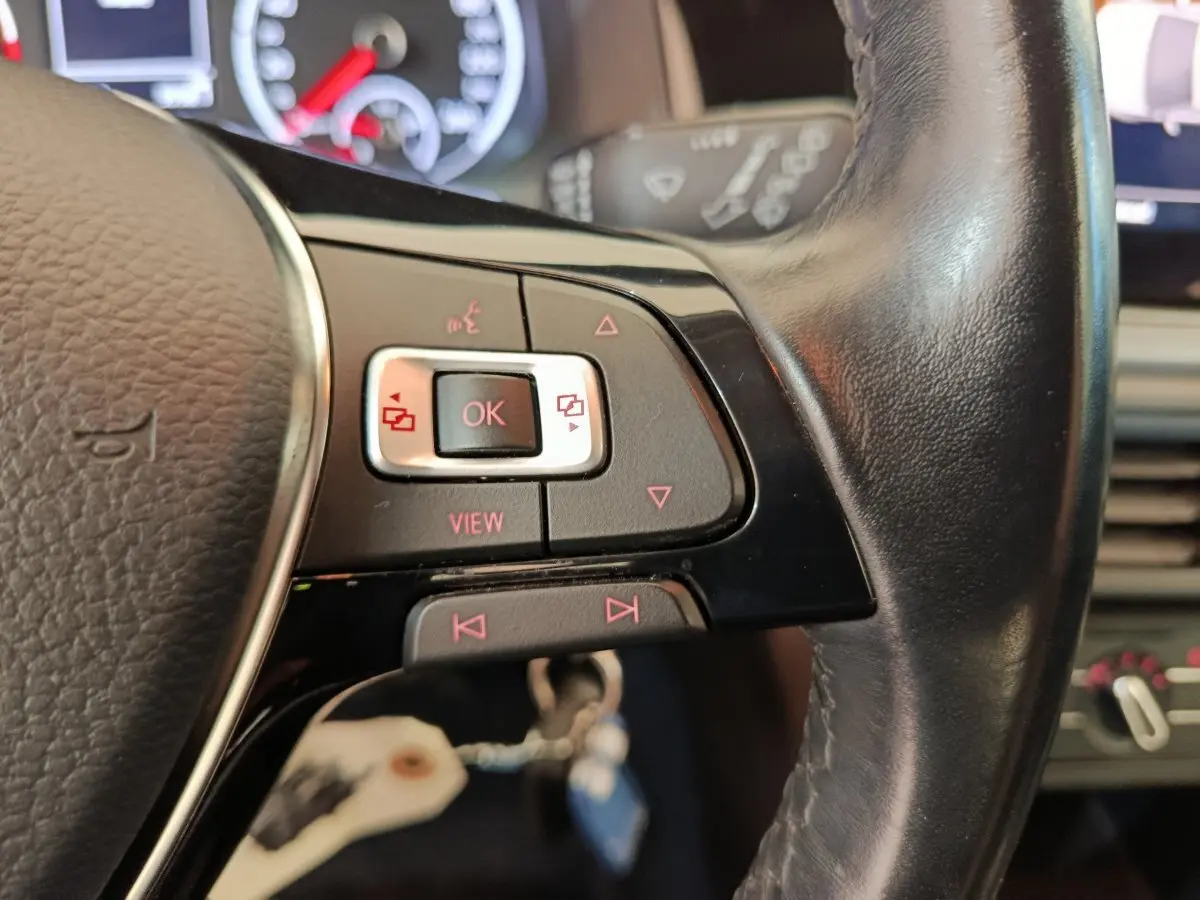 Gros plan sur les commandes gauche du volant cuir noir de la Volkswagen Polo blanche, tableau de bord en arrière-plan.