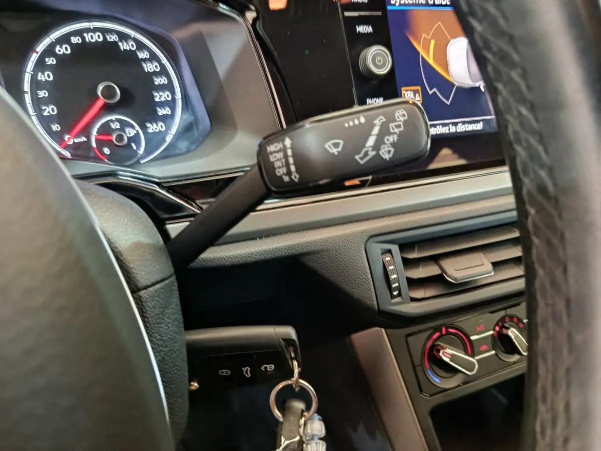 Vue rapprochée du tableau de bord et volant de la Volkswagen Polo blanche 2020, avec commandes d’essuie-glace et écran tactile visible.