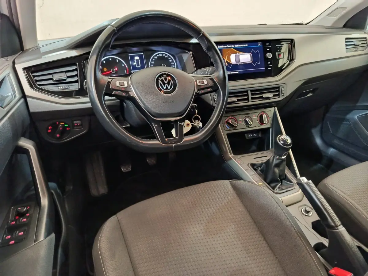 Vue intérieure avant de la Volkswagen Polo blanche 2020, tableau de bord avec écran tactile et volant cuir multifonctions.