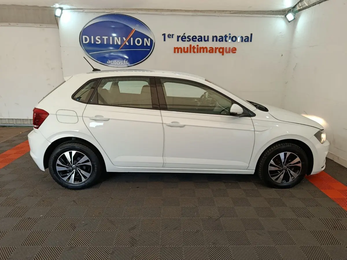 Profil droit d'une Volkswagen Polo blanche 2020 avec jantes alliage et logo Distinxion en arrière-plan.
