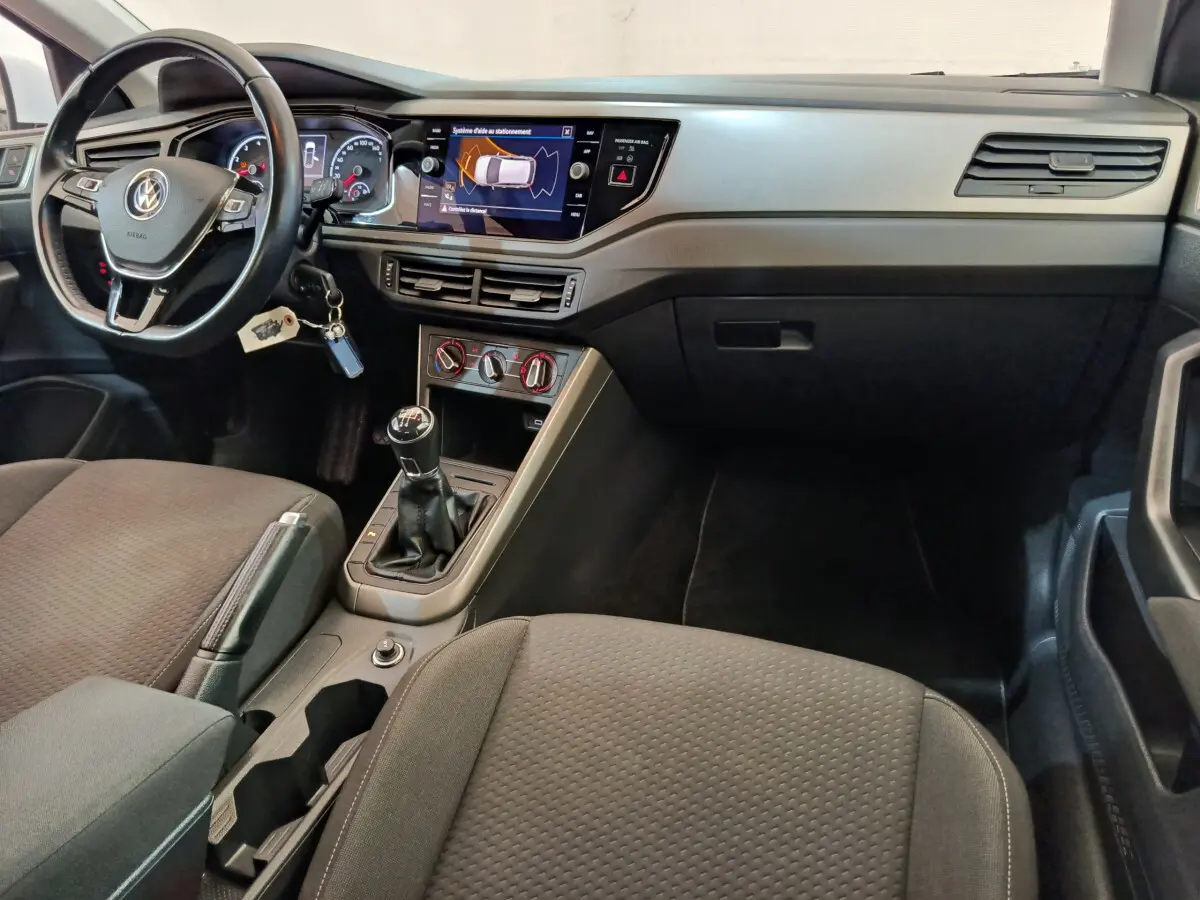 Intérieur avant de la Volkswagen Polo blanche 2020, tableau de bord avec écran tactile et boîte manuelle visible.