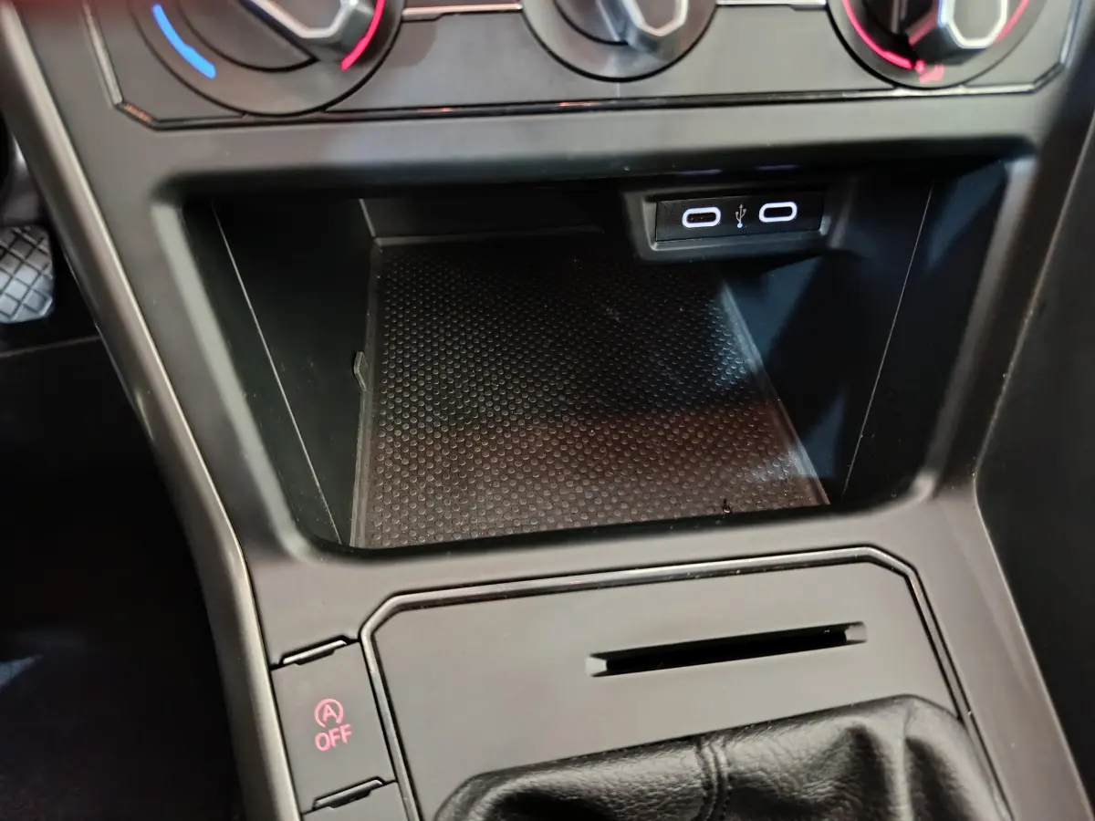 Gros plan sur la console centrale noire de la Volkswagen Polo blanche, montrant la zone de rangement et ports USB.
