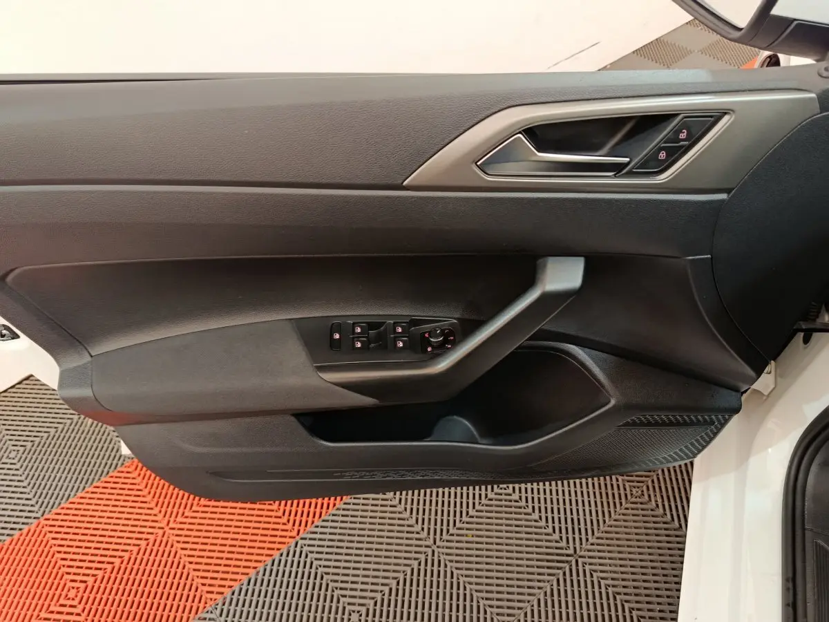 Vue rapprochée de la porte avant gauche noire d'une Volkswagen Polo blanche, avec commandes de vitres et serrure intégrées.