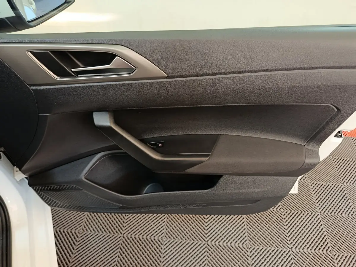 Vue rapprochée de la porte avant gauche noire d'une Volkswagen Polo blanche 2020, avec poignée intégrée et rangements.