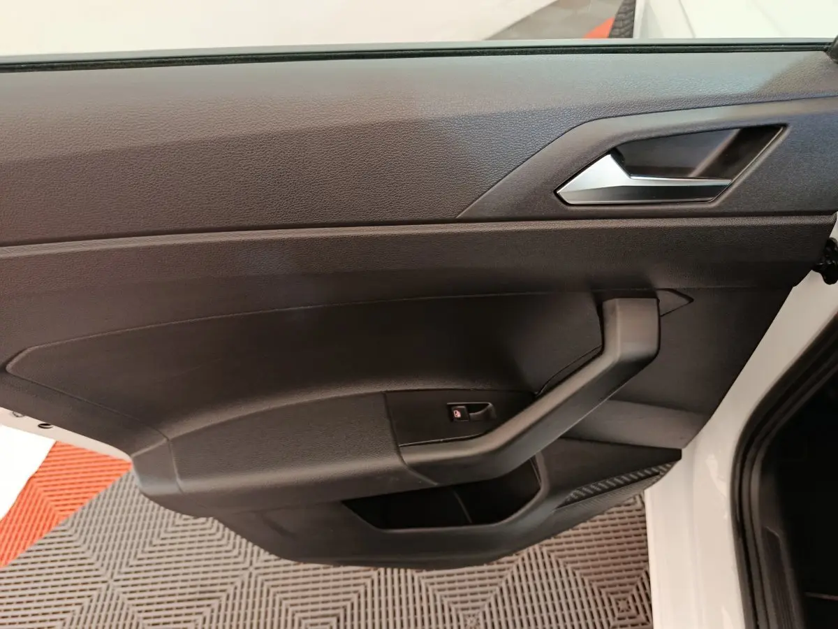 Gros plan sur la porte intérieure côté gauche noire d'une Volkswagen Polo blanche 2020, avec poignée et bouton de verrouillage.