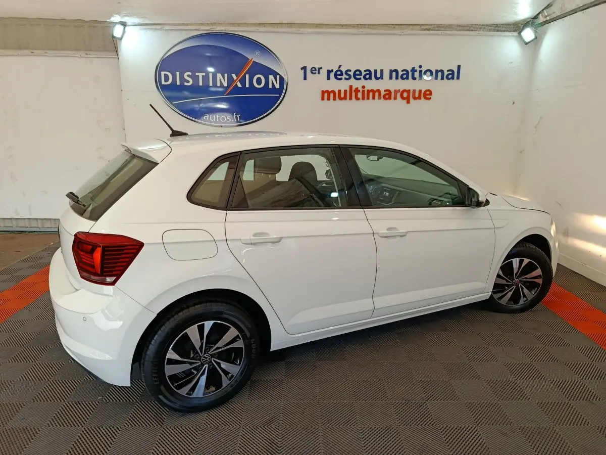 Volkswagen Polo blanche vue de profil côté gauche dans un showroom avec jantes noires et rouges arrière visibles.