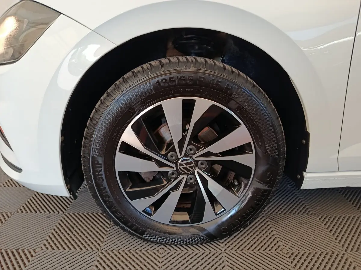 Gros plan sur la roue avant gauche d'une Volkswagen Polo blanche, jante alliage bicolore au design moderne.