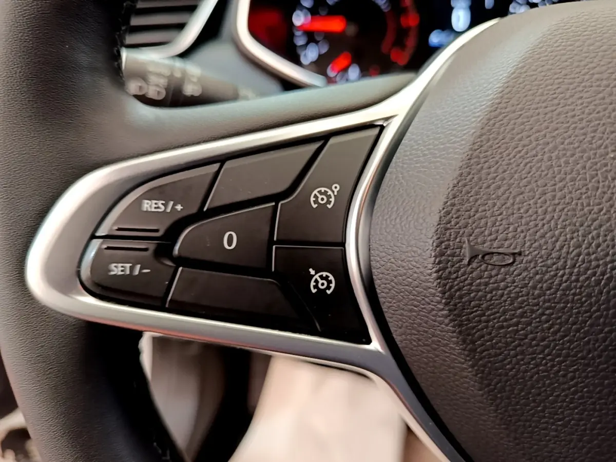 Gros plan sur les commandes de régulateur de vitesse au volant cuir noir d'une Renault Clio Business Blue dCi blanche.