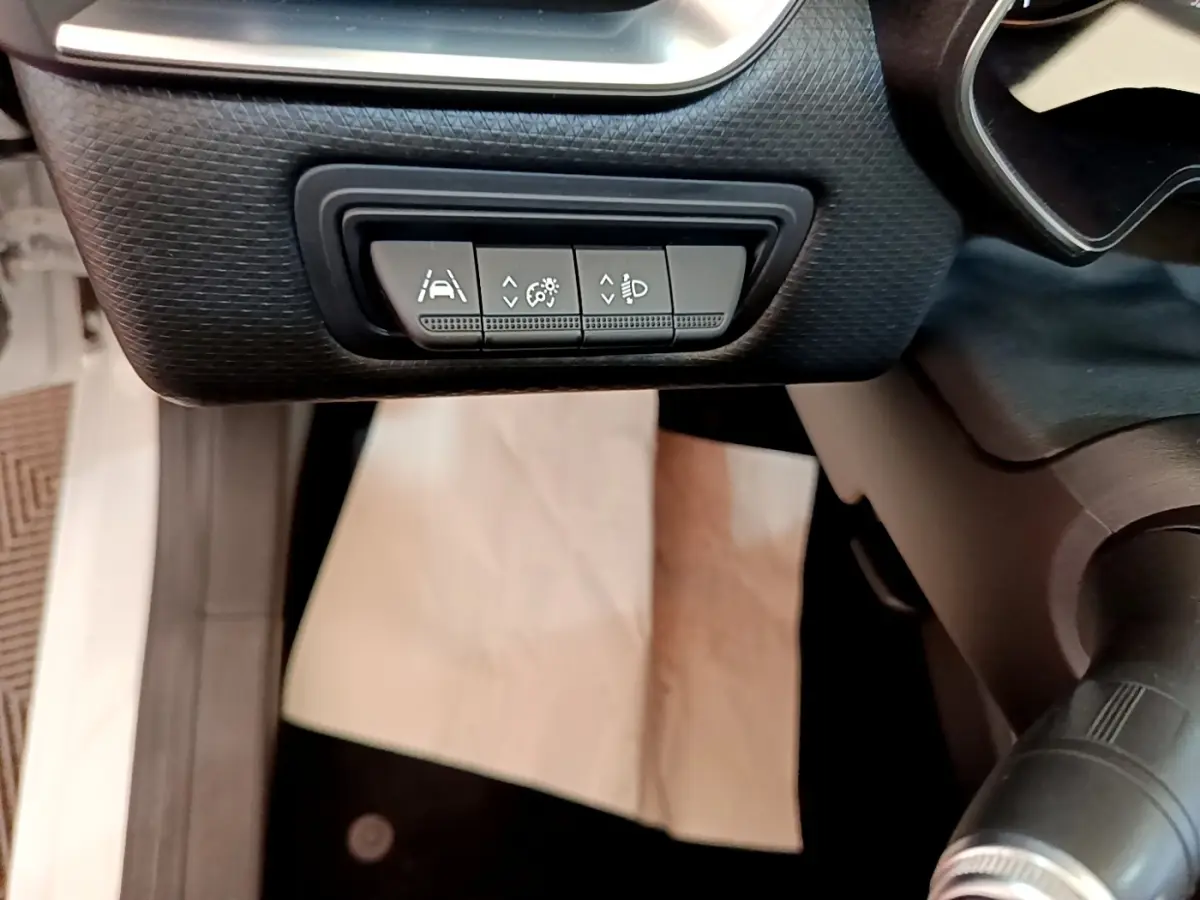 Gros plan sur les commandes d'assistance à la conduite sous le tableau de bord d'une Renault Clio blanche.
