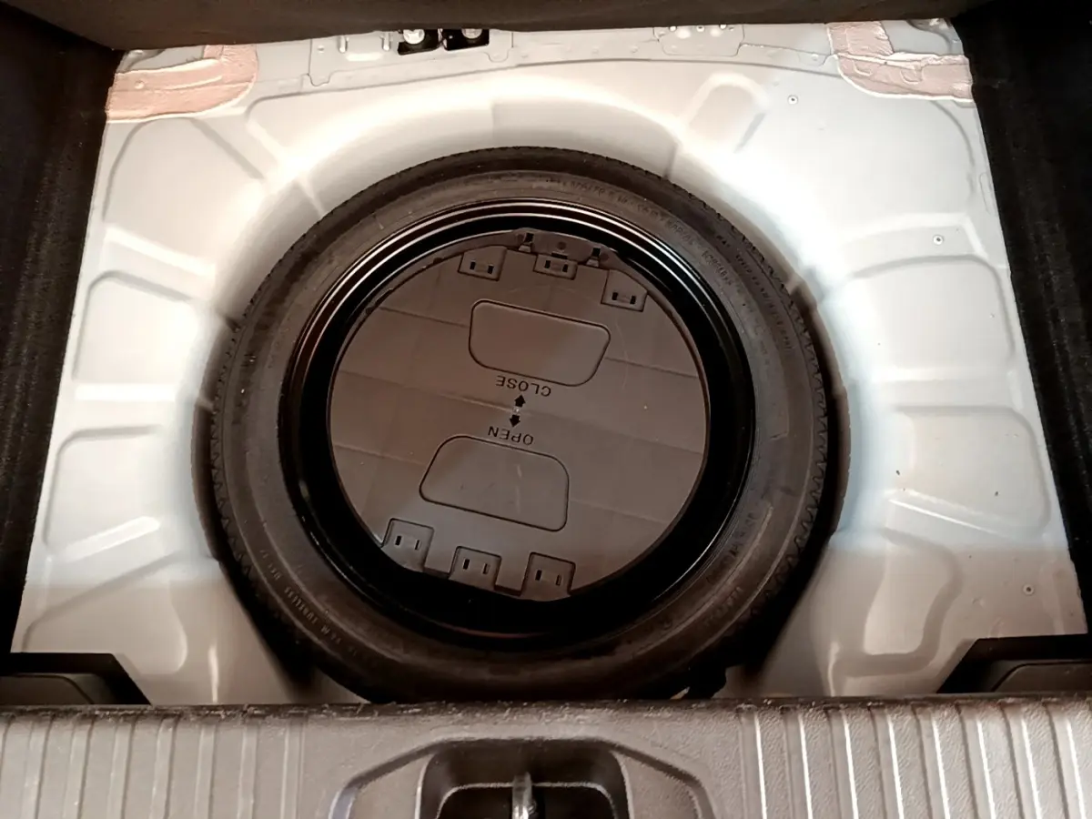 Vue plongeante sur la roue de secours noire dans le coffre blanc d'une Renault Clio Business Blue dCi 85 2020.