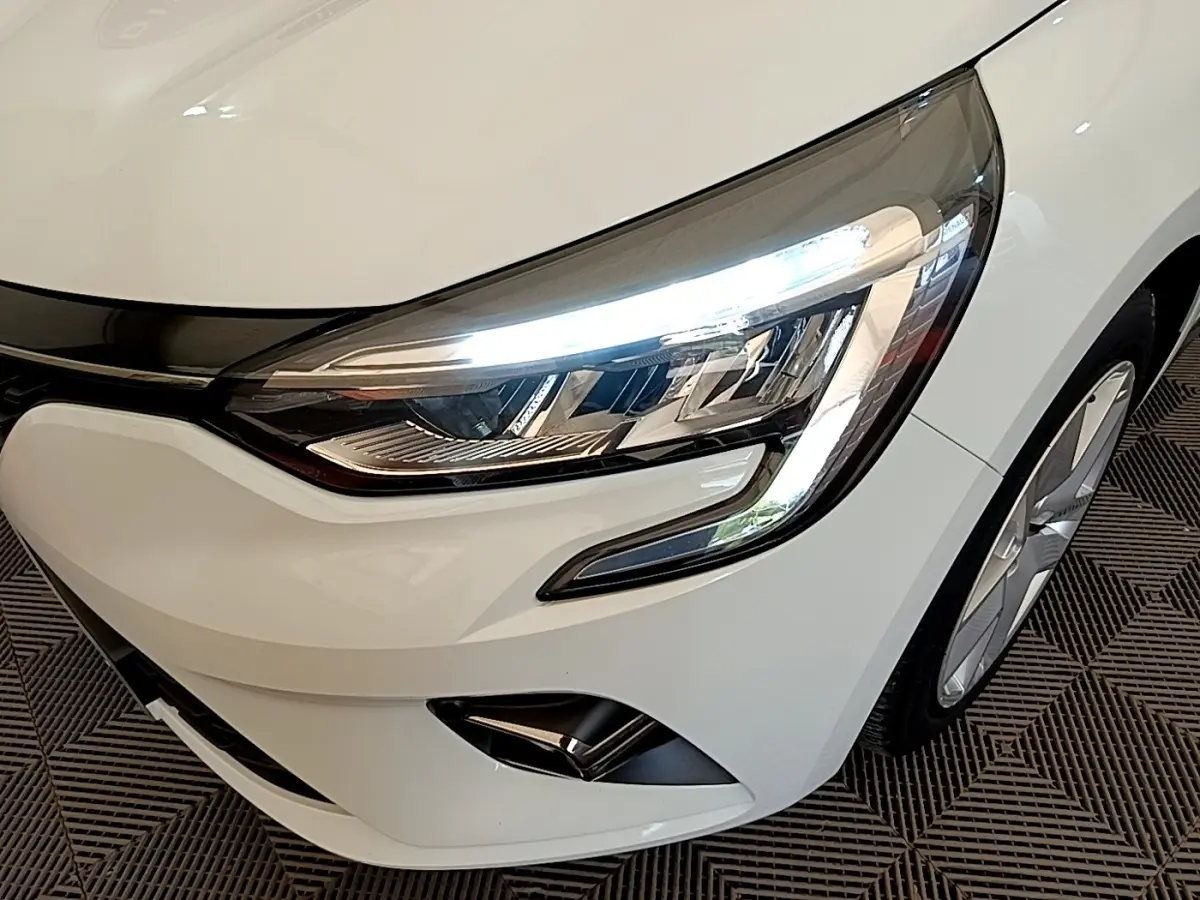 Gros plan sur l'avant droit blanc d'une Renault Clio 2020 avec phares LED allumés et jante visible.