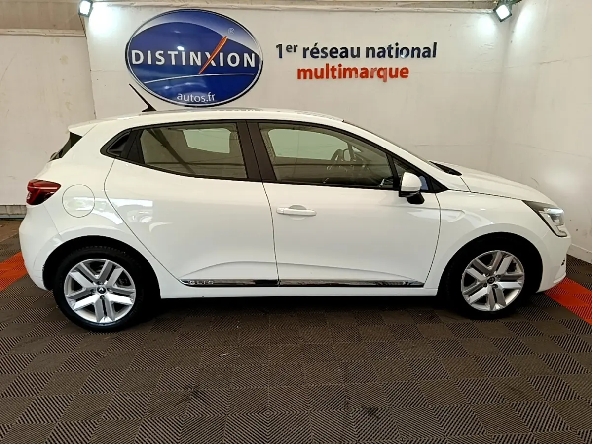 Profil droit d'une Renault Clio blanche 2020 Business Blue dCi, avec jantes alliage et logo Distinxion en arrière-plan.