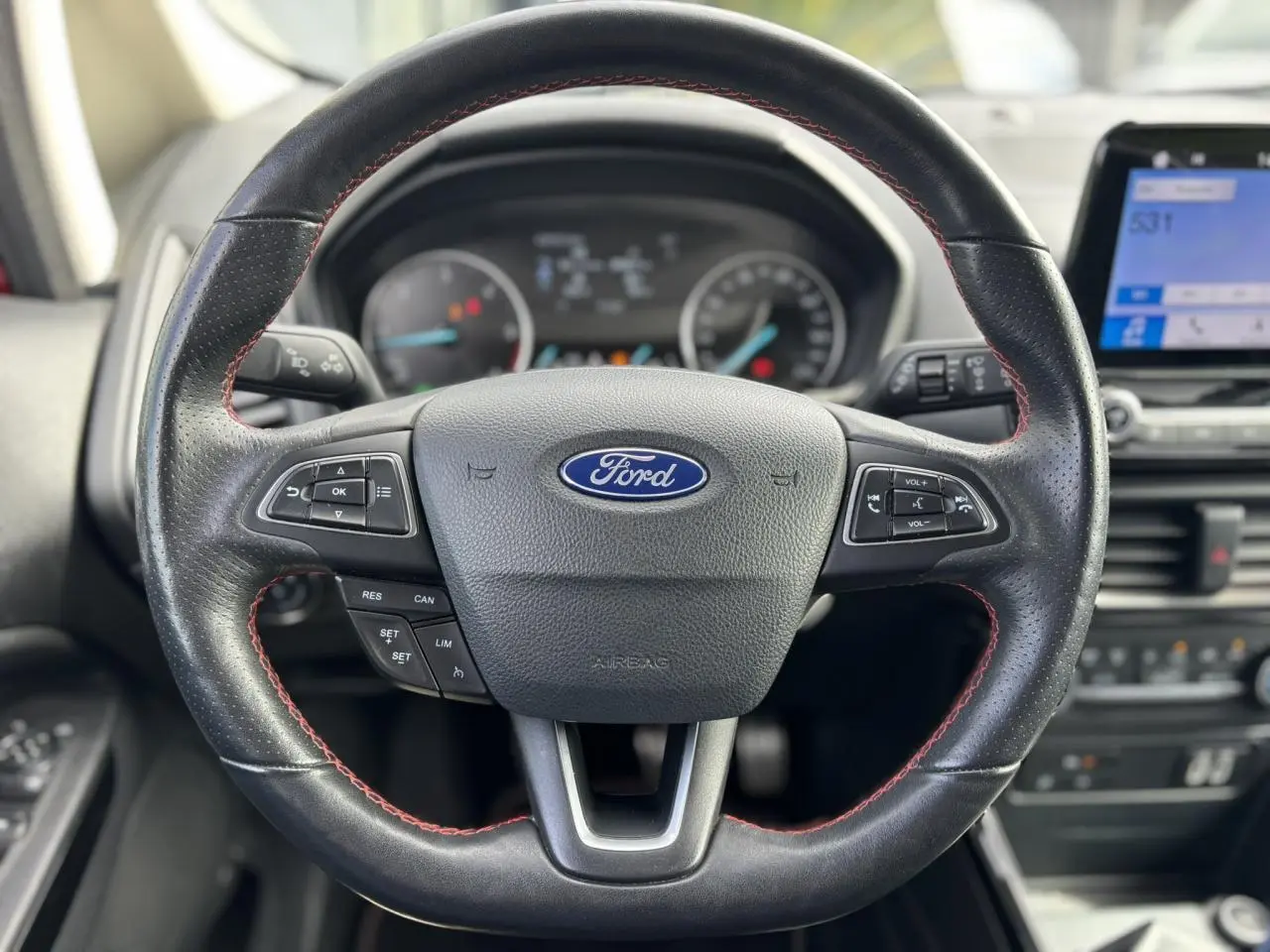 Volant en cuir perforé noir avec surpiqûres rouges du Ford Ecosport ST-Line, tableau de bord et écran tactile en arrière-plan.