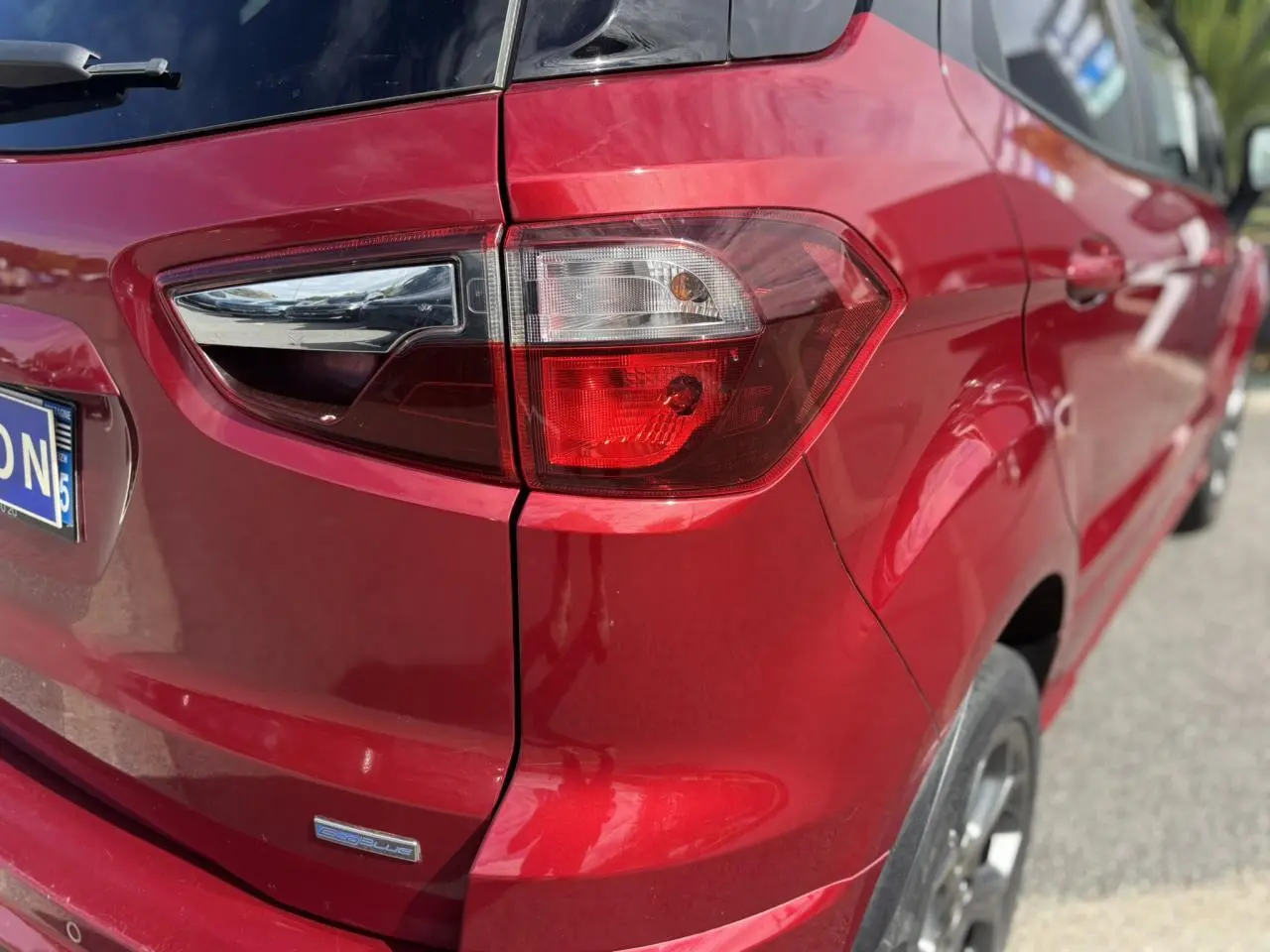Gros plan sur le feu arrière droit d'une Ford EcoSport rouge métallisée, soulignant la finition EcoBlue et la carrosserie brillante.