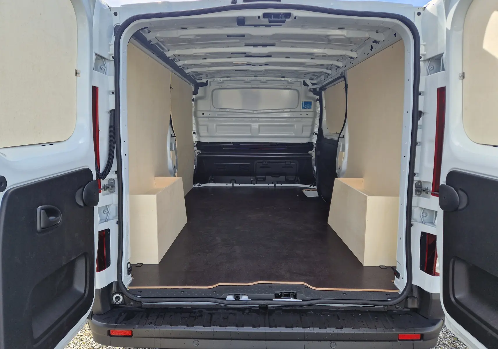 Vue arrière ouverte du Nissan Primastar blanc 2025, montrant l'intérieur vide avec aménagements bois latéraux du Pack Cargo.