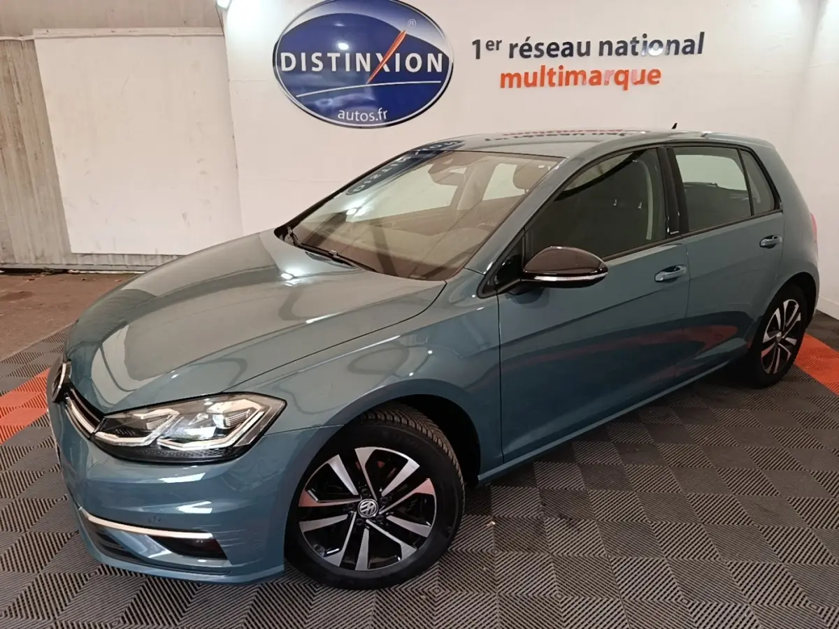 Volkswagen Golf bleu vue 3/4 avant droit, avec jantes noires et phares LED dans un showroom intérieur.
