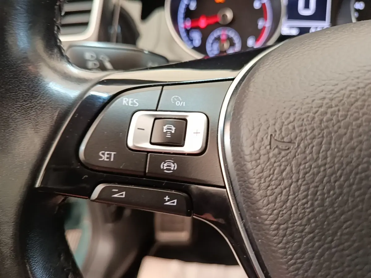 Gros plan sur le volant cuir multifonctions de la Volkswagen Golf bleu, avec commandes de régulateur de vitesse.