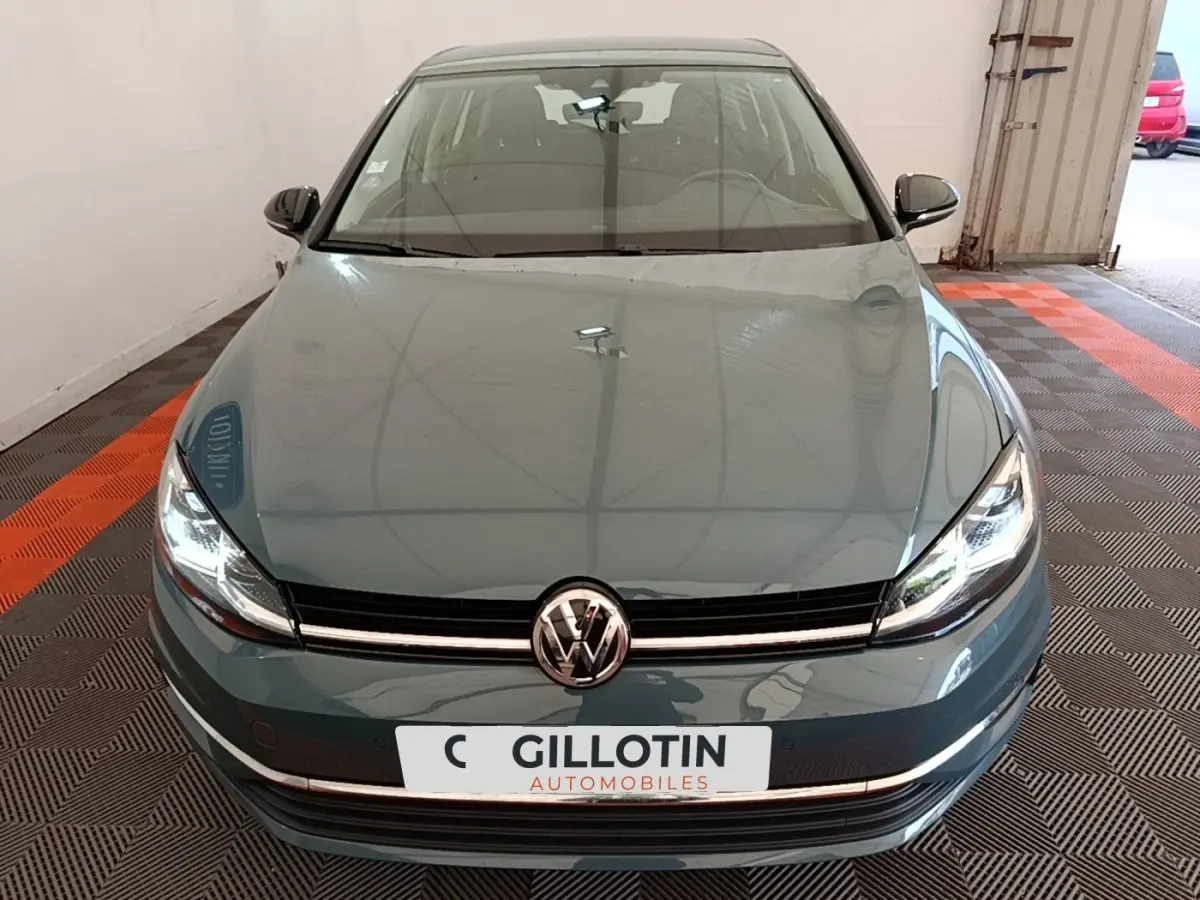 Vue avant d'une Volkswagen Golf bleu 2020 avec phares LED allumés dans un garage.