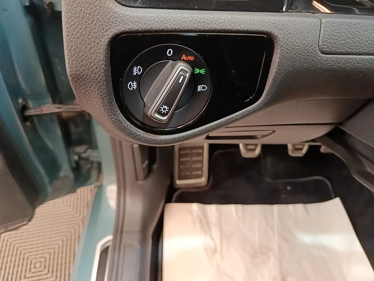 Gros plan sur le bouton de commande des phares à gauche du volant dans une Volkswagen Golf bleu, intérieur côté conducteur.