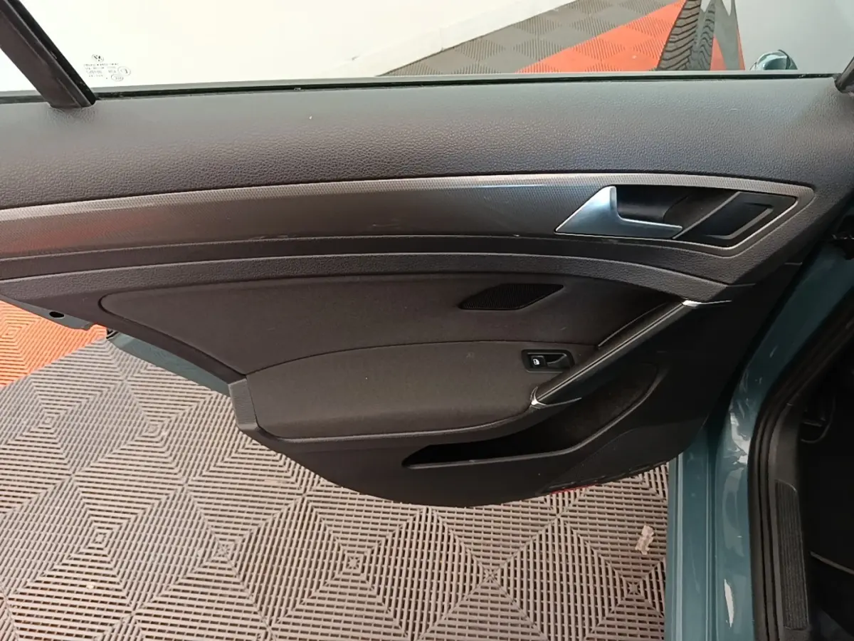 Vue intérieure de la porte avant gauche d’une Volkswagen Golf bleu 2020, avec panneau noir et poignée argentée.